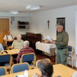 Mies seisomassa oikealla edessä pöydissä istumassa.