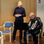 Mies laulaa seisten, istumassa haitarinsoittaja.