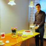 Pöydällä täytekakku. Mies seisomassa pöydän päässä kakkulapio kädessään.