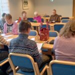 Ihmisiä istumassa pöydissä. lauluvihkot edessään.